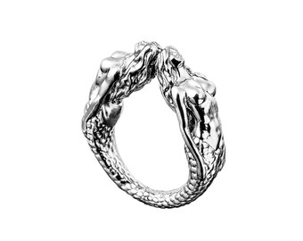 May include: A silver ring featuring two mermaids intertwined, their tails forming the band of the ring.