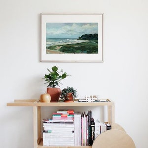 May include: A wooden rolling cart with two shelves, filled with books and magazines. The cart has a large wooden wheel on the right side. A framed painting of a seascape hangs on the wall behind the cart.