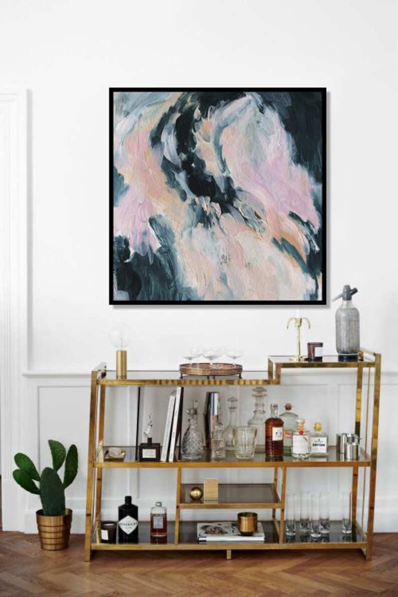 May include: A gold metal bar cart with glass shelves. The cart is filled with various bottles, glasses, and barware. A painting with abstract pink, white, and blue brushstrokes hangs on the wall above the cart.