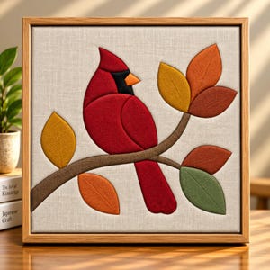 Puede incluir: Una pieza de arte mural cuadrada enmarcada que presenta un aplique de tela de un pájaro cardenal rojo posado en una rama marrón. El diseño incluye hojas texturizadas en tonos amarillo, naranja, óxido y verde sobre un fondo beige tipo lino.