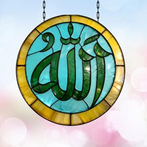 May include: A circular stained glass suncatcher featuring the Arabic calligraphy for Allah in deep green glass, set against a bright turquoise background, all enclosed within a golden yellow border and suspended by two metal chains.