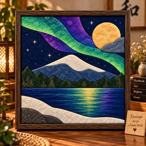 May include: A framed fabric art piece depicting a night landscape with a snow-capped mountain, a dark blue lake, and a vibrant green and purple aurora borealis in the sky. A large yellow moon and small stars are visible above the mountain range.