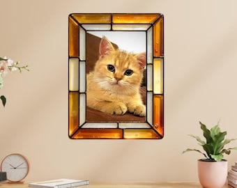 May include: A rectangular stained glass frame with a golden tabby kitten inside. The frame has a border of amber, white, and gold glass pieces. The kitten has large, round eyes and is resting on a brown surface.