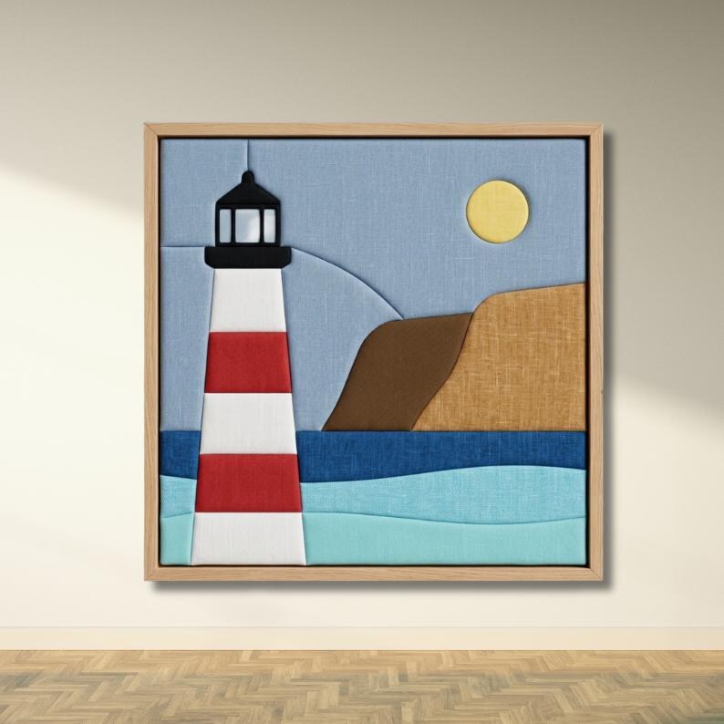 May include: A square fabric wall art piece in a light wood frame featuring a layered textile collage of a lighthouse with red and white stripes, a brown cliffside, a yellow sun, and a blue ocean scene composed of light and dark blue fabric.
