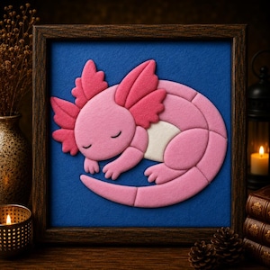 Peut inclure: Une œuvre d'art murale encadrée présentant une applique en feutrine superposée représentant un axolotl rose endormi avec des branchies plumeuses proéminentes. L'axolotl est placé sur un fond bleu profond, dans un cadre en bois brun foncé.