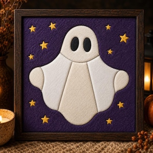 May include: A framed felt wall art piece featuring a white ghost with black oval eyes centered on a deep purple background. The ghost is surrounded by several small, yellow five-pointed stars scattered across the dark purple fabric surface.