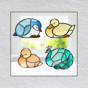 Könnte beinhalten: Vier Glasmalerei-Tierfiguren: ein Pinguin, eine Ente, ein Küken und ein Pfau. Der Pinguin ist blau und weiß, die Ente ist gelb, das Küken ist orange und der Pfau ist türkis und grün. Jede Figur hat eine schwarze Umrandung.