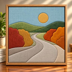 Puede incluir: Una pieza de arte mural de tela enmarcada de forma cuadrada que presenta un paisaje con un camino gris sinuoso, colinas verdes y un sol amarillo sobre un cielo azul claro. El primer plano muestra árboles de tela texturizada en tonos rojo, naranja y dorado.