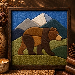 May include: A square framed fabric wall art piece featuring a layered textile collage of a brown bear walking across a green landscape. The background displays stylized mountains in shades of gray, white, and dark blue against a textured blue sky.