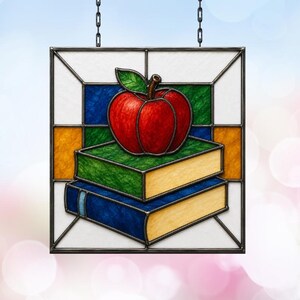 Peut inclure: Un panneau carré en vitrail représentant une pomme rouge avec une feuille verte posée sur deux livres empilés. Le livre du dessus a une couverture verte et celui du dessous une couverture bleue, tous deux avec des pages beige. Cadre en métal noir.