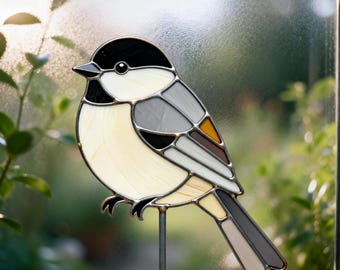 May include: Stained glass bird decoration featuring a chickadee design. The bird has a black head, cream-colored body, and gray and brown wings. It is mounted on a metal rod for display in a garden or as indoor decor.