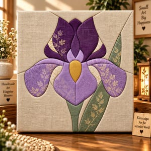 May include: A square fabric wall art piece featuring a central purple iris flower design. The flower is composed of textured fabric segments in shades of deep purple, light lavender, and yellow, with green leaf accents on a beige linen-like background.