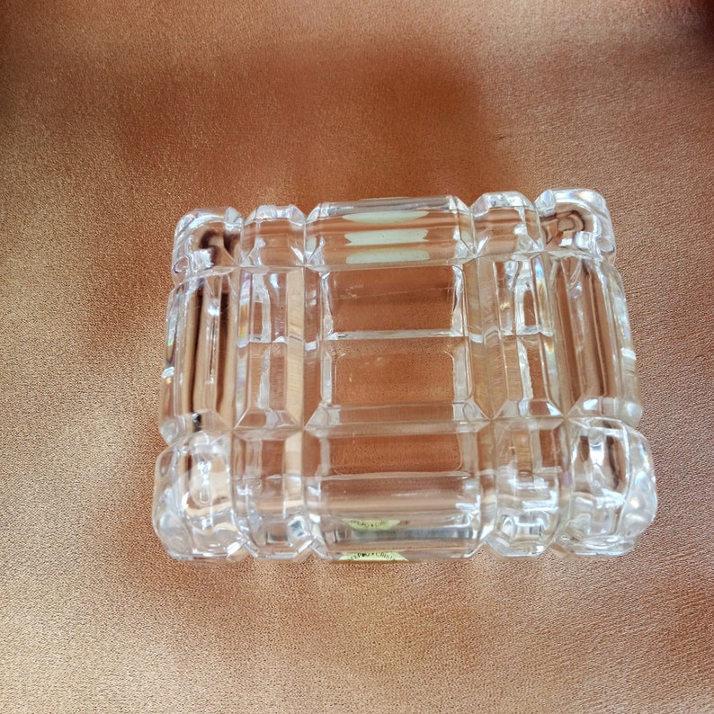 May include: A clear glass box with a square shape and a cut-glass design. The box has a small label on the bottom.