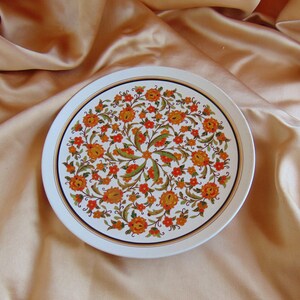 May include: A white ceramic dinner plate with a gold rim and a floral pattern in shades of orange, yellow, and green.