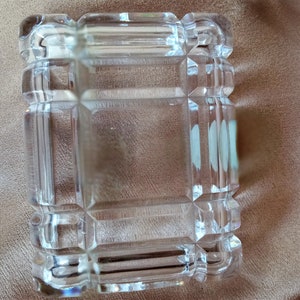 May include: A clear glass box with a decorative, geometric pattern. The box is empty and has a square shape.