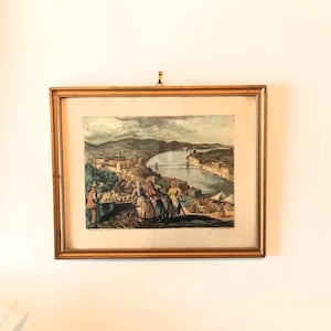 Może przedstawiać: Wizerunek vintage w ramie przedstawiający scenę miejską z rzeką i mostem. Wizerunek jest w złotej ramie i przedstawia grupę ludzi na pierwszym planie.