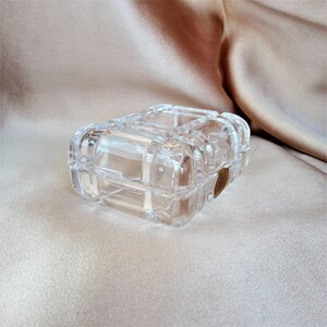 May include: A clear glass trinket box with a decorative, raised, geometric pattern. The box has a brass-colored latch.