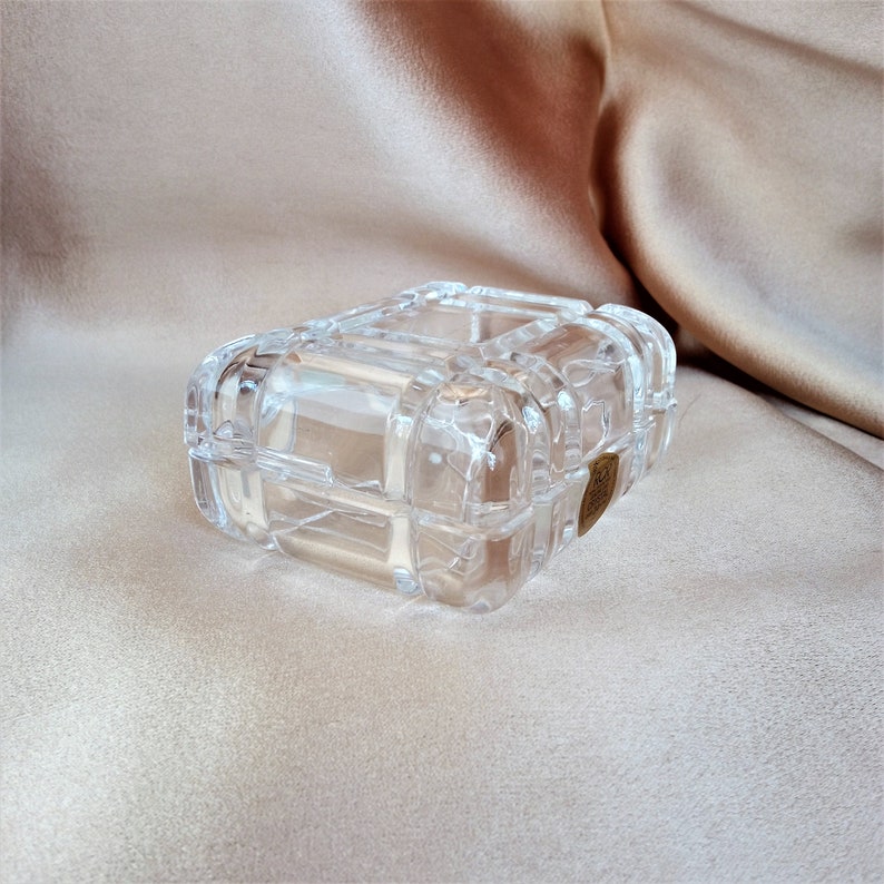 May include: A clear glass trinket box with a decorative, raised, geometric pattern. The box has a brass-colored latch.