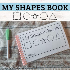 May include: A spiral-bound "My Shapes Book" with a light green and white marker. The book features the title and outlines of a square, circle, star, hexagon, and triangle. The book is open to a page with the same shapes and a "Name:" line.