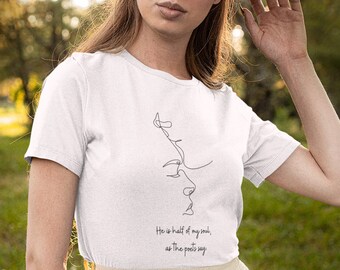May include: A white short-sleeved t-shirt featuring a black line art illustration of two faces in profile and the text "He is half of my soul, as the poets say" printed on the front, paired with a long, cream-coloured tulle skirt and a brown hat.