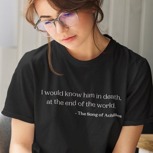 May include: A black short-sleeved t-shirt featuring white printed text that reads: I would know him in death, at the end of the world. - The Song of Achilles. The shirt has a crew neckline and is paired with white pants featuring thin black vertical stripes.