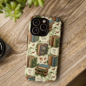 Puede incluir: Una funda de teléfono con un patrón repetido de libros antiguos, mariposas y elementos florales sobre un fondo verde claro. Los libros son de varios colores, algunos adornados con flores y follaje. La funda tiene un acabado brillante.