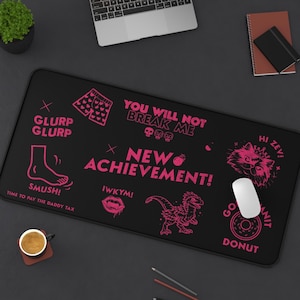 May include: Black rectangular mousepad with pink graphics and text. The design includes a foot, a dinosaur, a cat, and phrases like "NEW ACHIEVEMENT!" and "YOU WILL NOT BREAK ME".