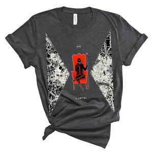 Op de afbeelding: Donkergrijs T-shirt met een witte en zwarte afbeelding van een persoon die op een rode troon zit. De afbeelding bevat de tekst "Six of Crows" en "A Novel".