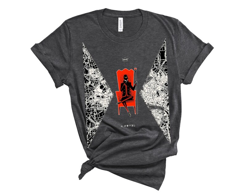 Op de afbeelding: Donkergrijs T-shirt met een witte en zwarte afbeelding van een persoon die op een rode troon zit. De afbeelding bevat de tekst "Six of Crows" en "A Novel".