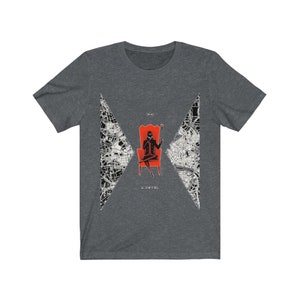 Op de afbeelding: Een donker grijs t-shirt met een zwart-witte afbeelding van een persoon die op een rode troon zit met een kaartontwerp op de achtergrond. De tekst "The Devil" is onder de afbeelding gedrukt.