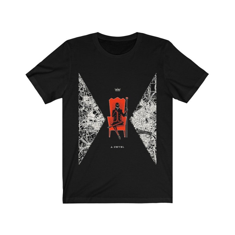 Op de afbeelding: Zwart T-shirt met een witte afbeelding van een persoon die op een rode troon zit met een kroon en een scepter. De afbeelding is omgeven door een wit kaartontwerp. De tekst "A NOVEL" staat onder de afbeelding.