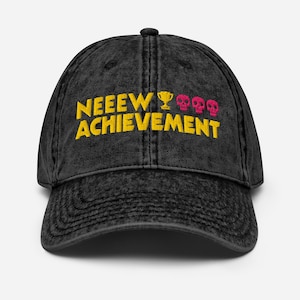 Può includere: Un cappellino da baseball nero con effetto lavaggio acido, caratterizzato dalla scritta ricamata in giallo NEEEW ACHIEVEMENT, accompagnata da una piccola icona di trofeo gialla e tre icone di teschi rosa centrate sul pannello frontale.