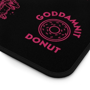 K&ouml;nnte beinhalten: Schwarzes Mousepad mit einem rosa Donut-Motiv und den Worten "GODDAMNIT DONUT". Das Mousepad hat auch ein rosa Dinosaurier-Motiv in der oberen linken Ecke. Die R&auml;nder sind schwarz.