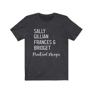 Peut inclure: T-shirt gris fonc&eacute; avec texte blanc. Le texte indique "SALLY GILLIAN FRANCES & BRIDGET" empil&eacute; verticalement, avec "Practical Magic" en cursive en dessous. Le t-shirt est fait d'une mati&egrave;re douce.