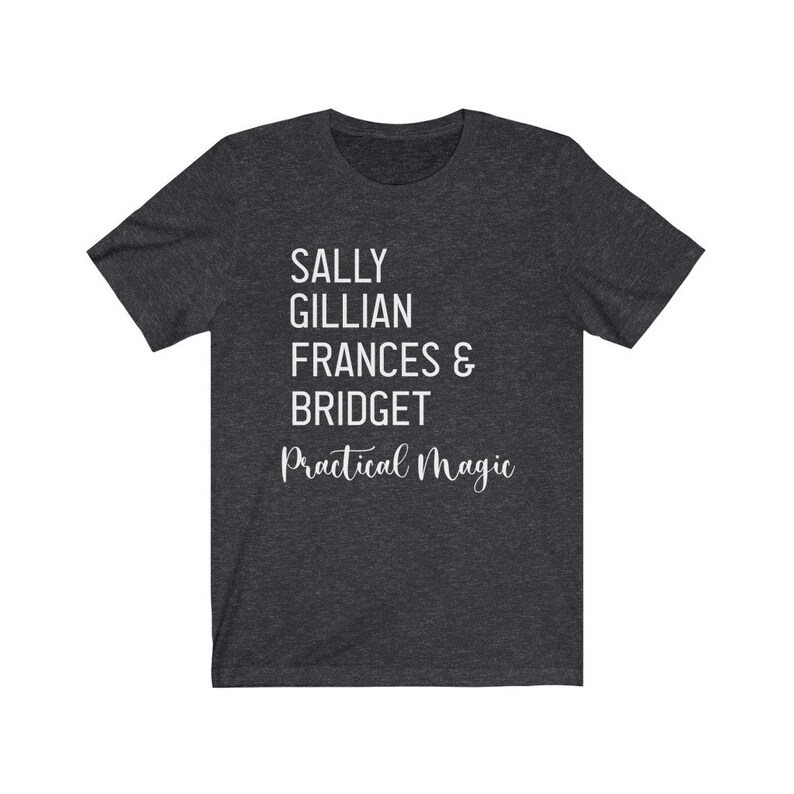 Peut inclure: T-shirt gris fonc&eacute; avec texte blanc. Le texte indique "SALLY GILLIAN FRANCES & BRIDGET" empil&eacute; verticalement, avec "Practical Magic" en cursive en dessous. Le t-shirt est fait d'une mati&egrave;re douce.