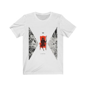 Op de afbeelding: Wit T-shirt met een zwart-wit ontwerp van een stadskaart. Het ontwerp toont een silhouet van een persoon die op een rode troon zit, een staf vasthoudt en een kroon draagt. De tekst "A NOVEL" is onder het ontwerp gedrukt.