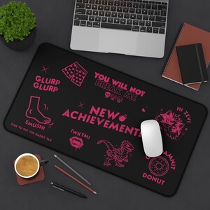 K&ouml;nnte beinhalten: Schwarzes rechteckiges Mousepad mit rosa Grafiken und Text. Der Text enth&auml;lt S&auml;tze wie "You Will Not Break Me" und "New Achievements". Weitere Grafiken sind ein Fu&szlig;, ein Dinosaurier und ein Donut.