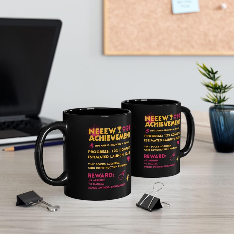 May include: Two black ceramic mugs with the text "NEEEW ACHIEVEMENT" in pink and yellow. The mugs have a side quest and reward details printed on them, including "Tiny Socks Acquired" and "+3 Appetite."