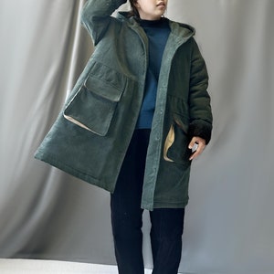 May include: A long, green corduroy coat with a hood and large pockets. The coat has a brown corduroy trim on the pockets and cuffs.