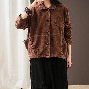 May include: A brown corduroy jacket with a button-up front and two patch pockets. The jacket is worn over a pair of black corduroy trousers.