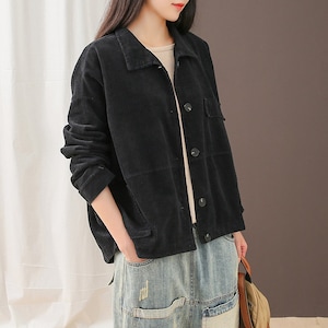 May include: A black corduroy jacket with a button-up front and a patch pocket on the right side. The jacket is worn over a white shirt and blue jeans.