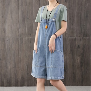 May include: A light blue denim overall dress with adjustable straps and large pockets. The dress has a relaxed fit and is perfect for casual wear.