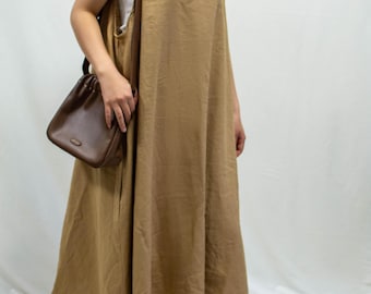 Peut inclure: Une femme portant une robe en lin sans manches de couleur beige clair avec un sac seau en cuir marron.