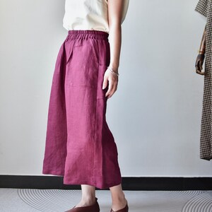 Puede incluir: Una camiseta sin mangas color crema combinada con pantalones de pierna ancha burdeos. Los pantalones tienen bolsillos y cintura el&aacute;stica. Zapatos planos de cuero marr&oacute;n completan el conjunto. Un maniqu&iacute; es visible en el fondo.