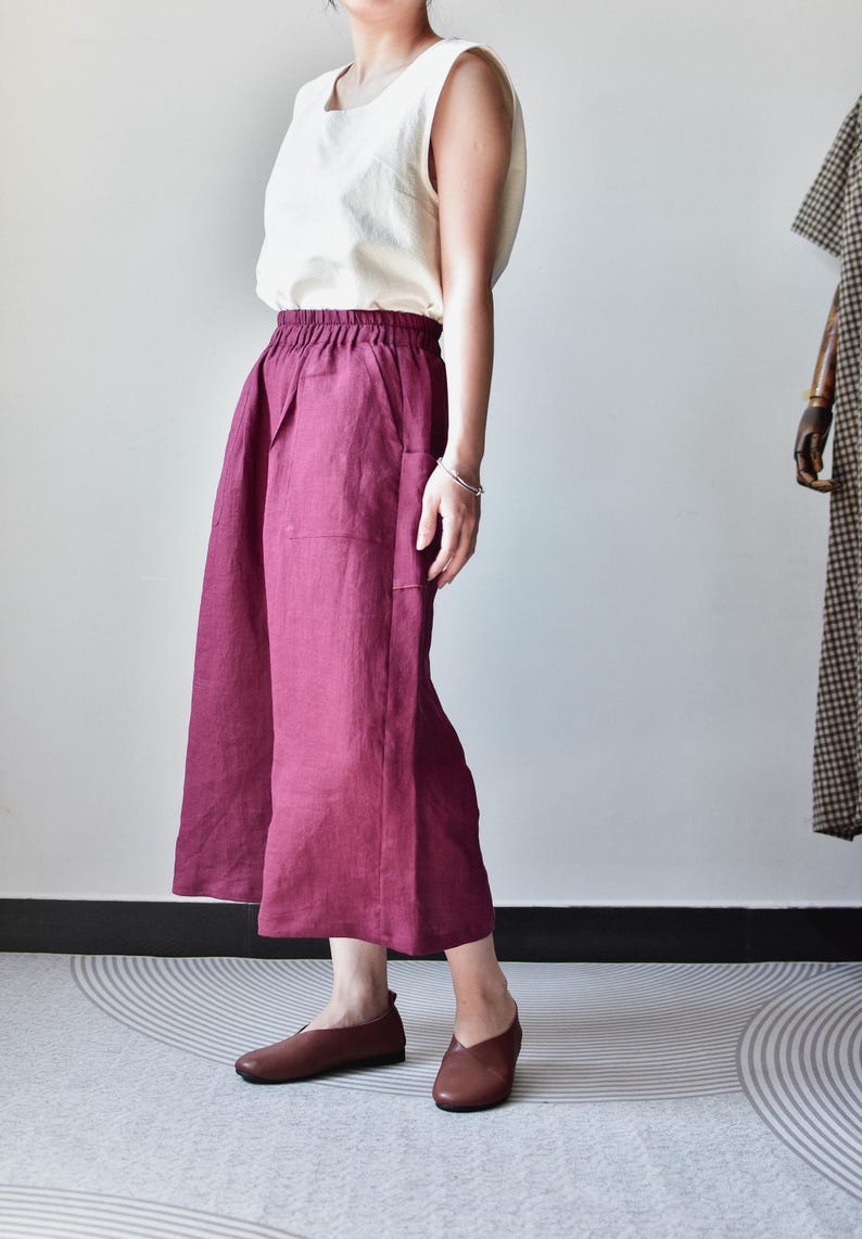 Puede incluir: Una camiseta sin mangas color crema combinada con pantalones de pierna ancha burdeos. Los pantalones tienen bolsillos y cintura el&aacute;stica. Zapatos planos de cuero marr&oacute;n completan el conjunto. Un maniqu&iacute; es visible en el fondo.