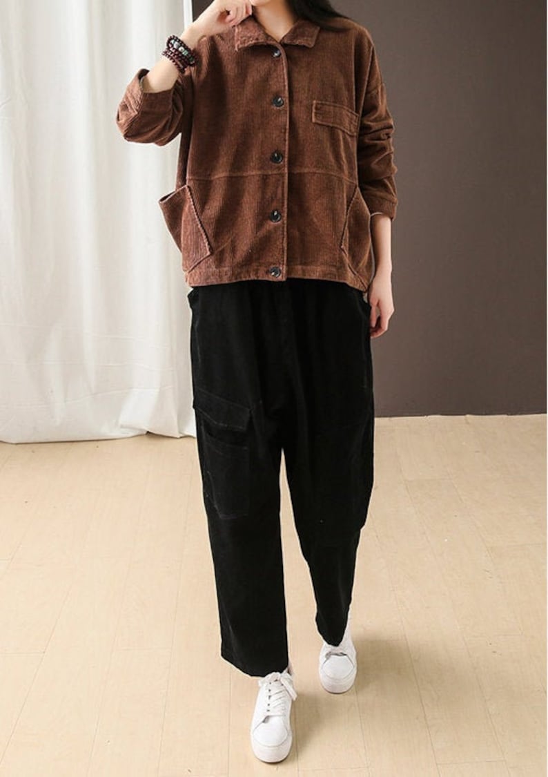 May include: A brown corduroy jacket with a button-up front and two patch pockets. The jacket is worn over a pair of black corduroy trousers.