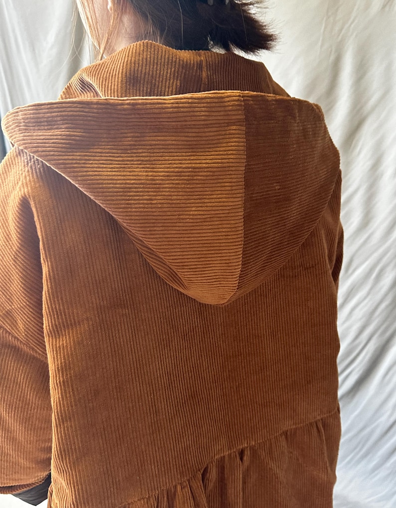 May include: A brown corduroy hooded jacket with a long, loose fit. The jacket has a drawstring hood and a relaxed, casual style.
