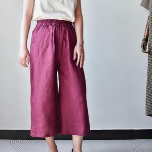 Puede incluir: Una persona con una camiseta sin mangas color crema y pantalones de pierna ancha burdeos. Los pantalones tienen cintura el&aacute;stica y bolsillos. La persona lleva zapatos de cuero marr&oacute;n. El atuendo es sencillo e informal.