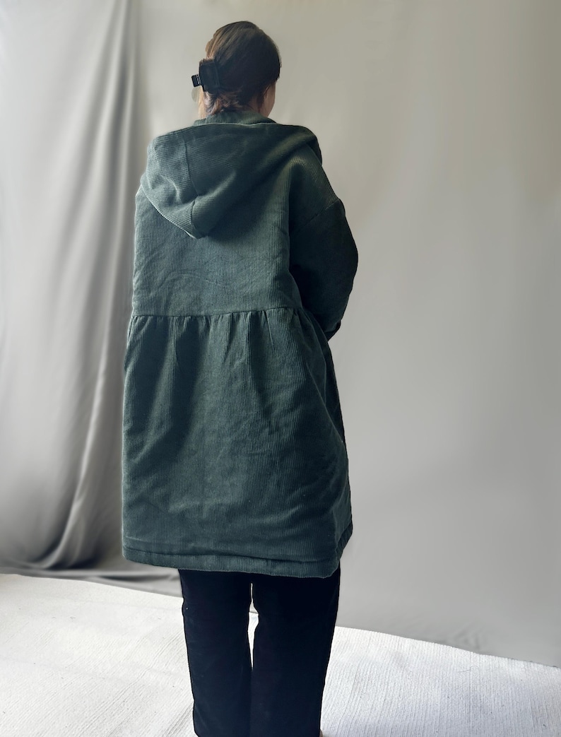 May include: A dark green corduroy hooded jacket with a cinched waist and long sleeves.