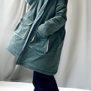 May include: A long, green corduroy jacket with a hood and large pockets. The jacket has a zipper closure and a button closure.